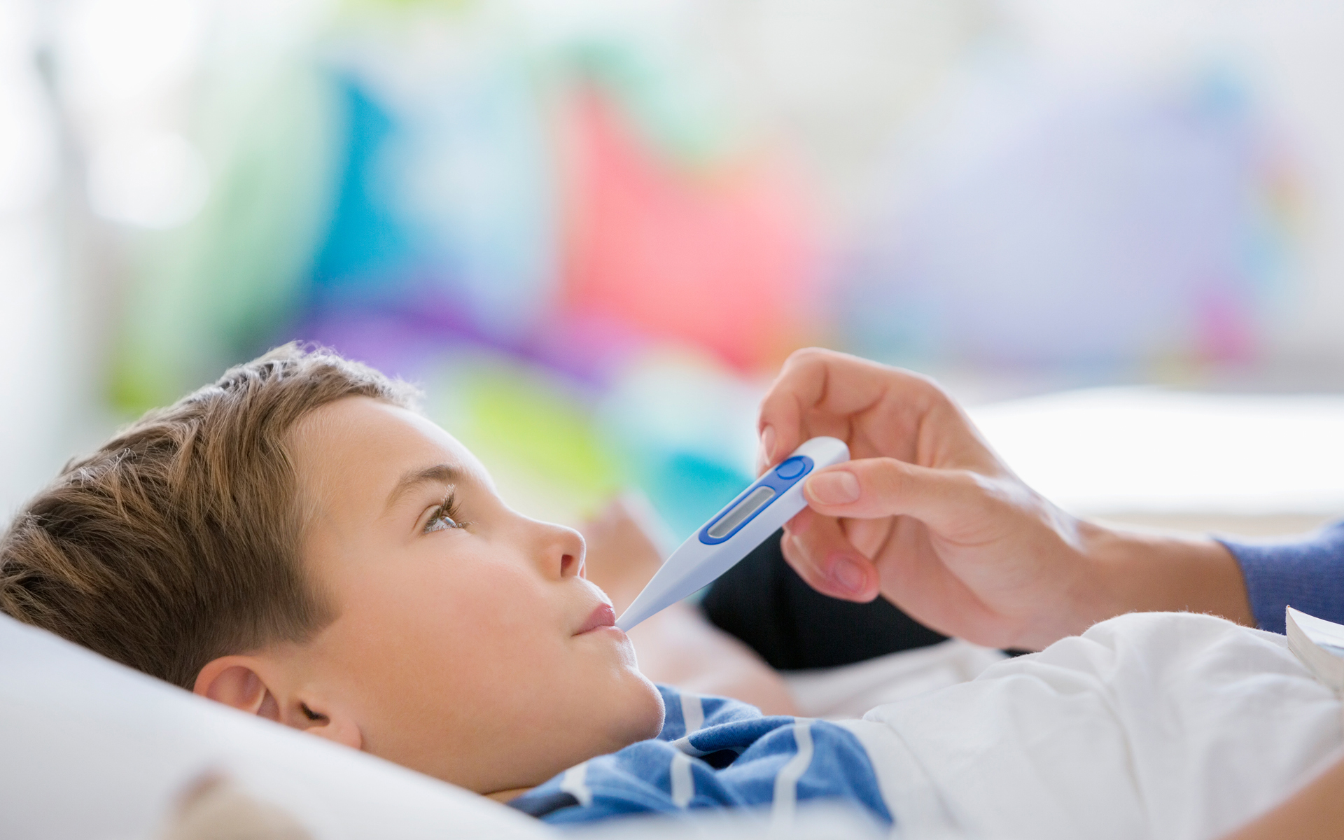 Boy in bed having his temperature taken by caretaker.